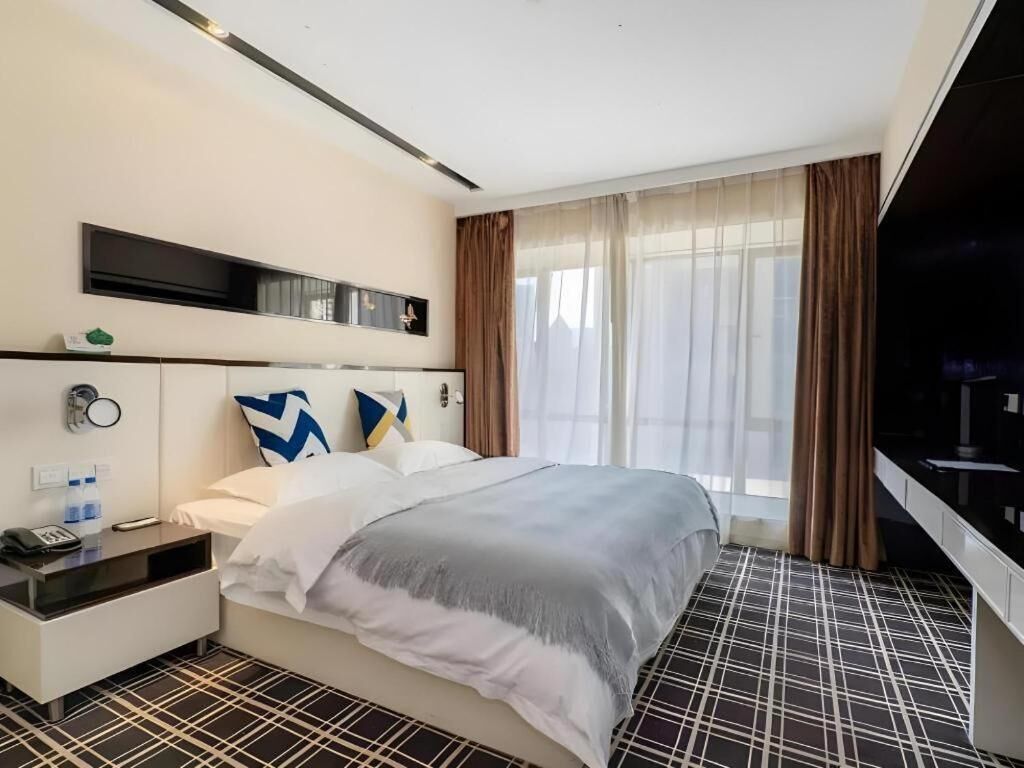 Una habitación de hotel moderna con una cama grande, una mesita de noche con teléfono y artículos de aseo, un televisor de pantalla plana y una ventana con cortinas.