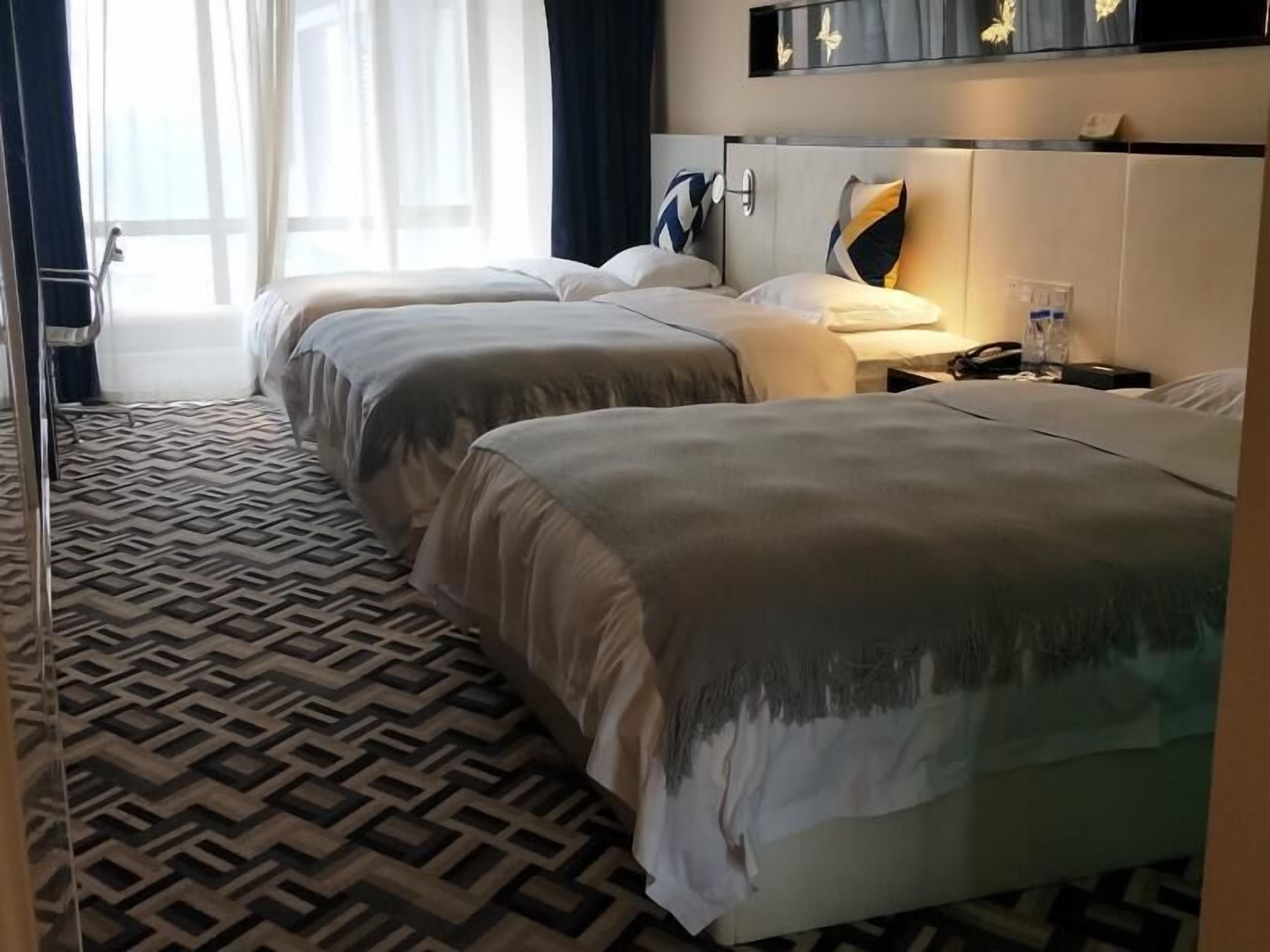 Una habitación de hotel con dos camas, alfombra estampada y una mesita de noche con lámpara.