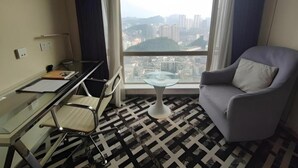 A hotel room with a desk, chair, and a view of the city through a large window. - Greentree Alliance Hotel Guiyang Huaguo Community Central Business Zone (Guiyang)