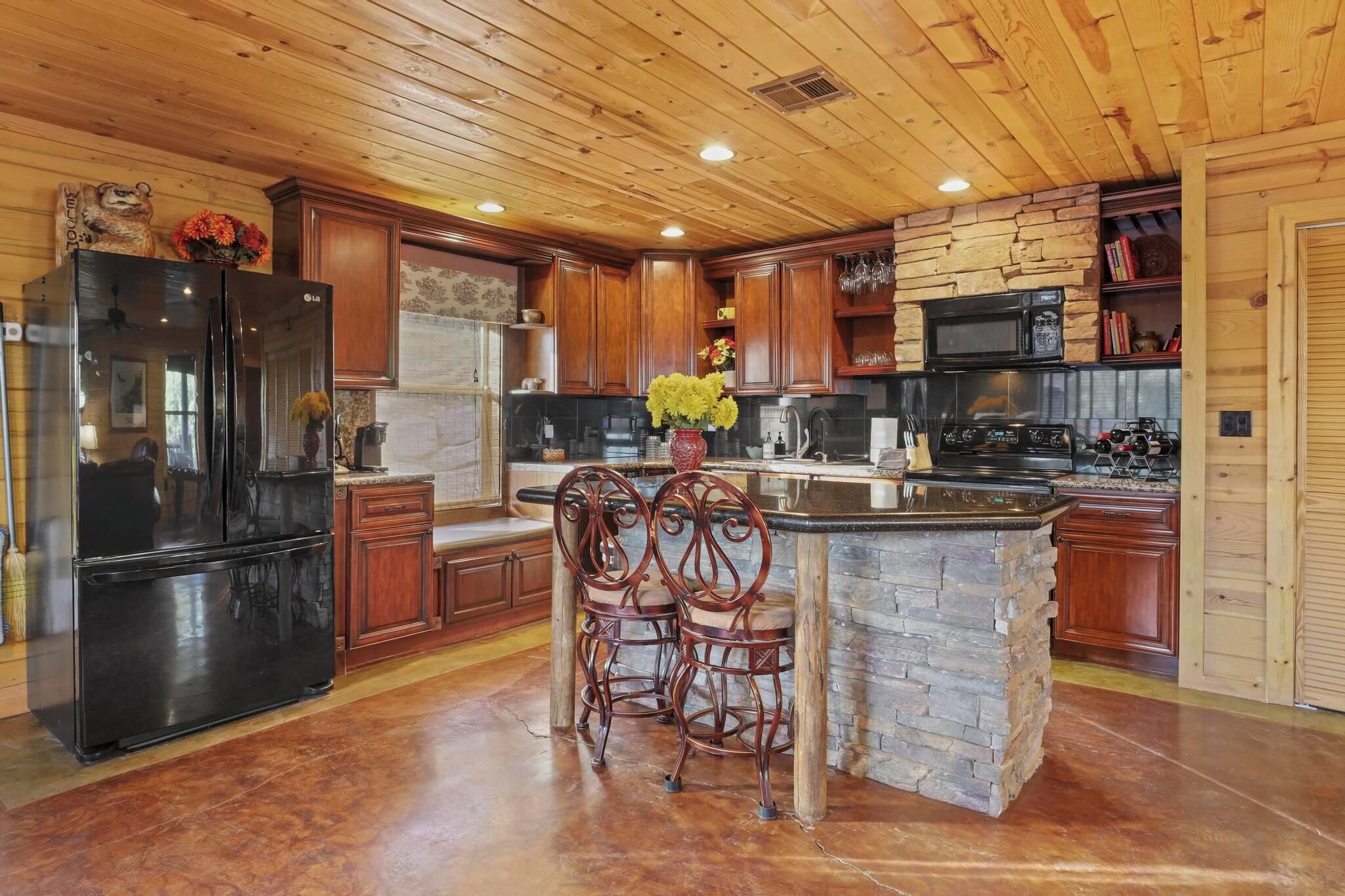 A kitchen with wooden cabinets, a black refrigerator, a stone island, and two bar stools.