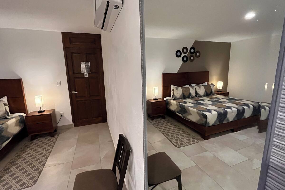 Une chambre d’hôtel comprenant un lit, une chaise, une table de chevet, une lampe, une porte et un climatiseur fixé au mur.