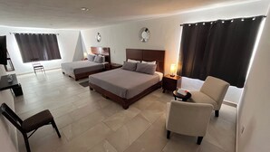 Habitació d'hotel amb dos llits, un escriptori, una cadira i una taula petita amb una làmpada.