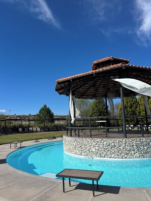 A swimming pool with a stone wall, a covered seating area, and a bench. - Pedernal Hotel (San Miguel de Allende)