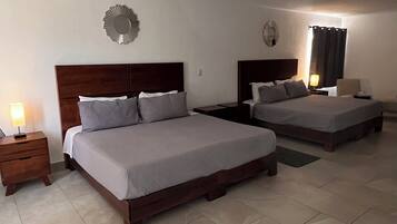 Quarto de hotel com duas camas, uma mesa de cabeceira com abajur e uma cadeira.