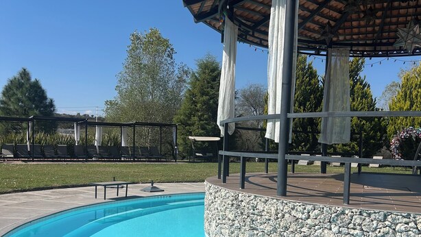Una piscina amb un marc de pedra, una zona de seients coberta i una pèrgola amb llums penjades.