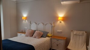 Ein Schlafzimmer mit einem Bett, Nachttischen, einem Sessel, einer Klimaanlage und Wandleuchten.