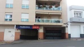 Un edificio de varios pisos con entrada a un estacionamiento, un letrero de servicio de estacionamiento y un balcón con plantas en macetas.