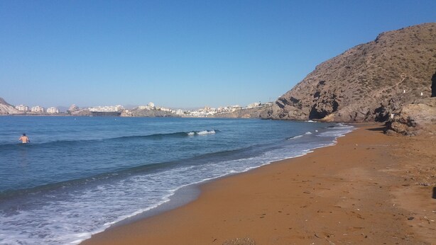 Ein Strand mit einer felsigen Klippe und einem strahlend blauen Himmel.