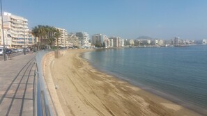 Un paisaje urbano costero con una playa arenosa, un paseo marítimo y edificios de gran altura.