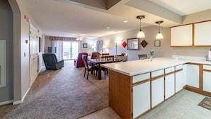 A spacious kitchen with a central island, a dining area with chairs, and a living room with a sofa and a TV. - 2 Bedroom, 2 Bathroom Walk-in Golf Condo with Covered Balcony, Indoor Pool Access (Branson)