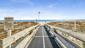 A wooden boardwalk leading to a beach with a sign listing beach rules.
