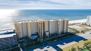 A high-rise hotel with multiple floors, a parking lot, and a view of the ocean.