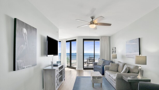 A modern living room with a flat-screen TV, a ceiling fan, and a sofa.