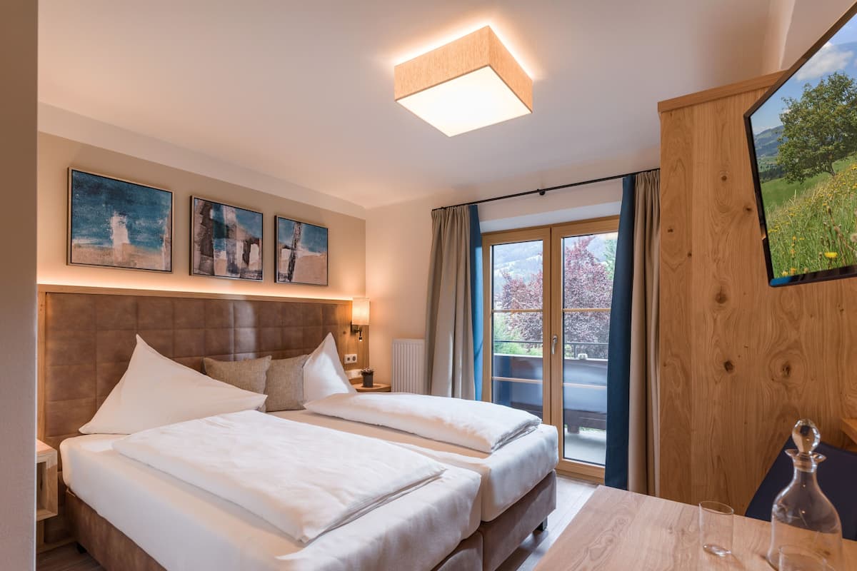 Habitación de hotel con dos camas, cabecera de madera, ventana grande con vistas a la vegetación y un televisor de pantalla plana montado en la pared.