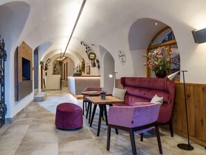 A cozy interior with a plush red sofa, a wooden table, and a pink ottoman. - Alpen Glück Hotel Unterm Rain garni (Kirchberg in Tirol)