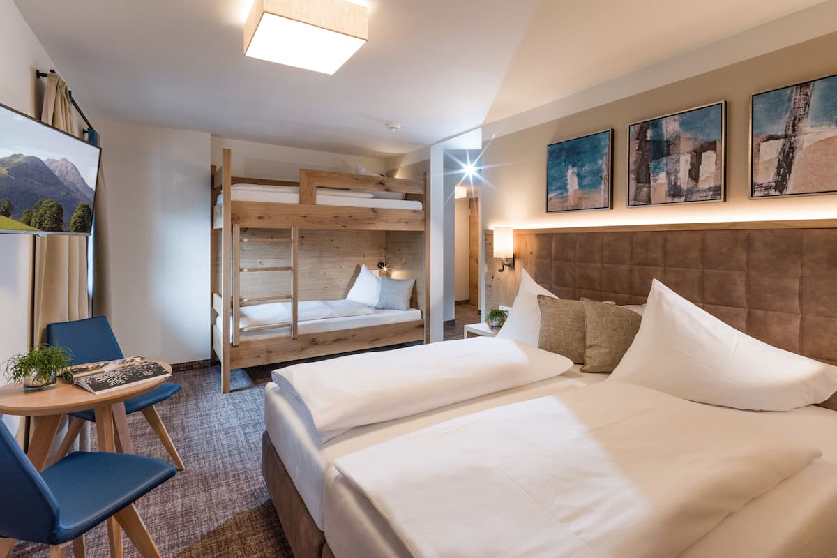 Una habitación de hotel moderna con literas, un escritorio con silla, un televisor de pantalla plana y obras de arte en las paredes.