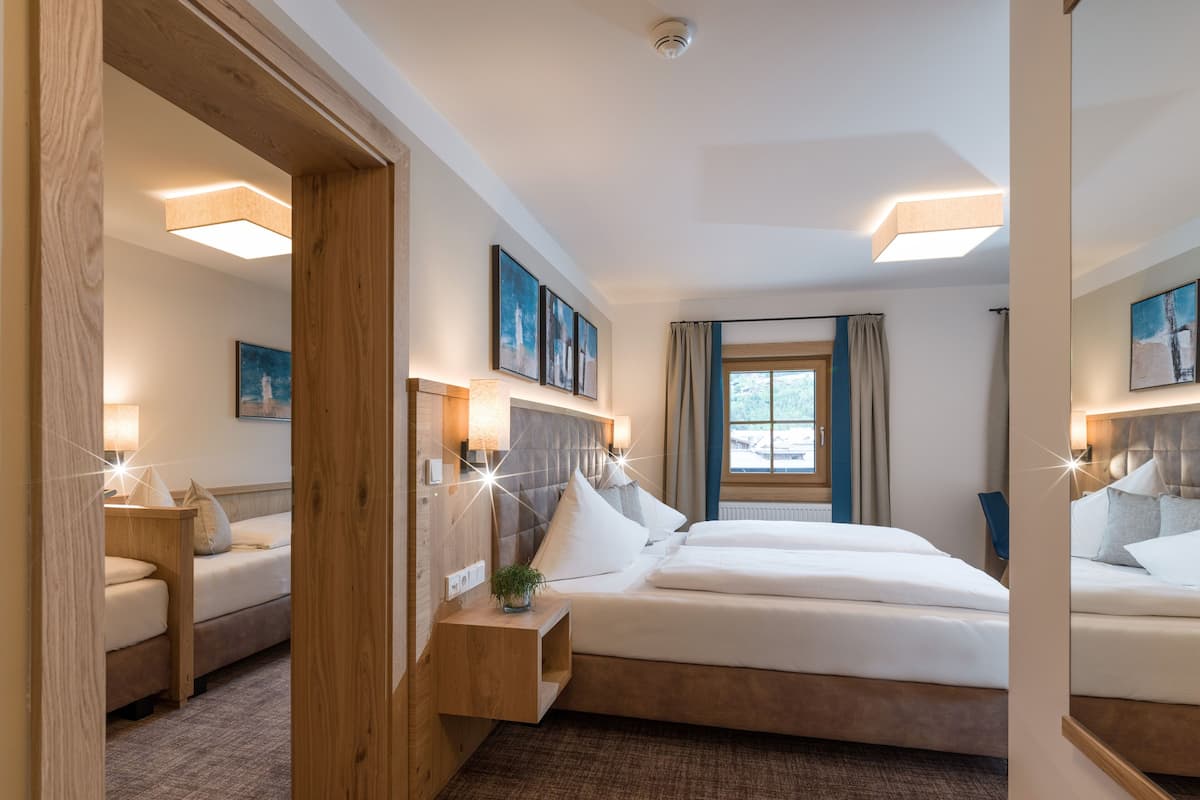 Una habitación de hotel con una cama grande, una cama más pequeña, una mesita de noche y una ventana con cortinas.