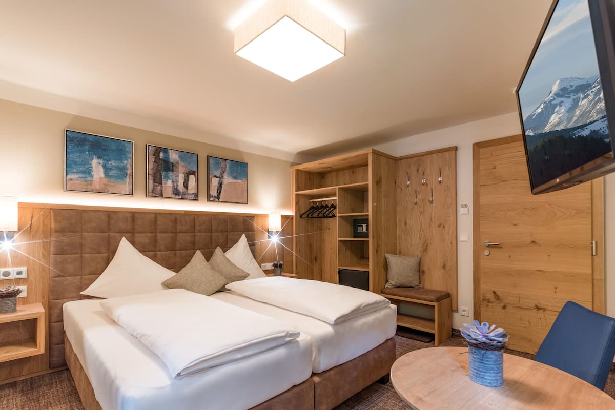 Una habitación de hotel con una cama grande, cabecero de madera, un televisor montado en la pared y una mesita redonda con un florero.