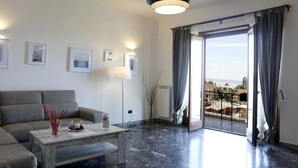 Un salon moderne avec un canapé gris, une table basse agrémentée d’objets décoratifs, un lampadaire et une vue dégagée sur l’extérieur grâce à une grande porte-fenêtre coulissante.