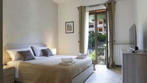 Une chambre à coucher avec un lit, des tables de chevet, une télévision et un balcon avec des rideaux.