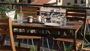 Une table à manger installée à l’extérieur, avec des chaises, un pot d’orchidée et, en arrière-plan, une vue sur des maisons et des montagnes.