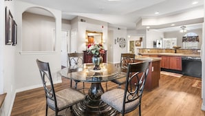 A dining area with a glass table and chairs, a vase with flowers, and a kitchen in the background. - Branson 2BR • Roll-In Shower • Near Aquarium, Tanger & Dining (Branson)