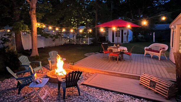 Een terras met buitenmeubilair, een vuurkorf en lichtslingers.