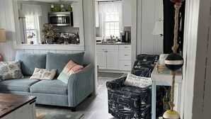 Een woonkamer met een bank, fauteuil en salontafel. In de achtergrond is een keuken te zien.