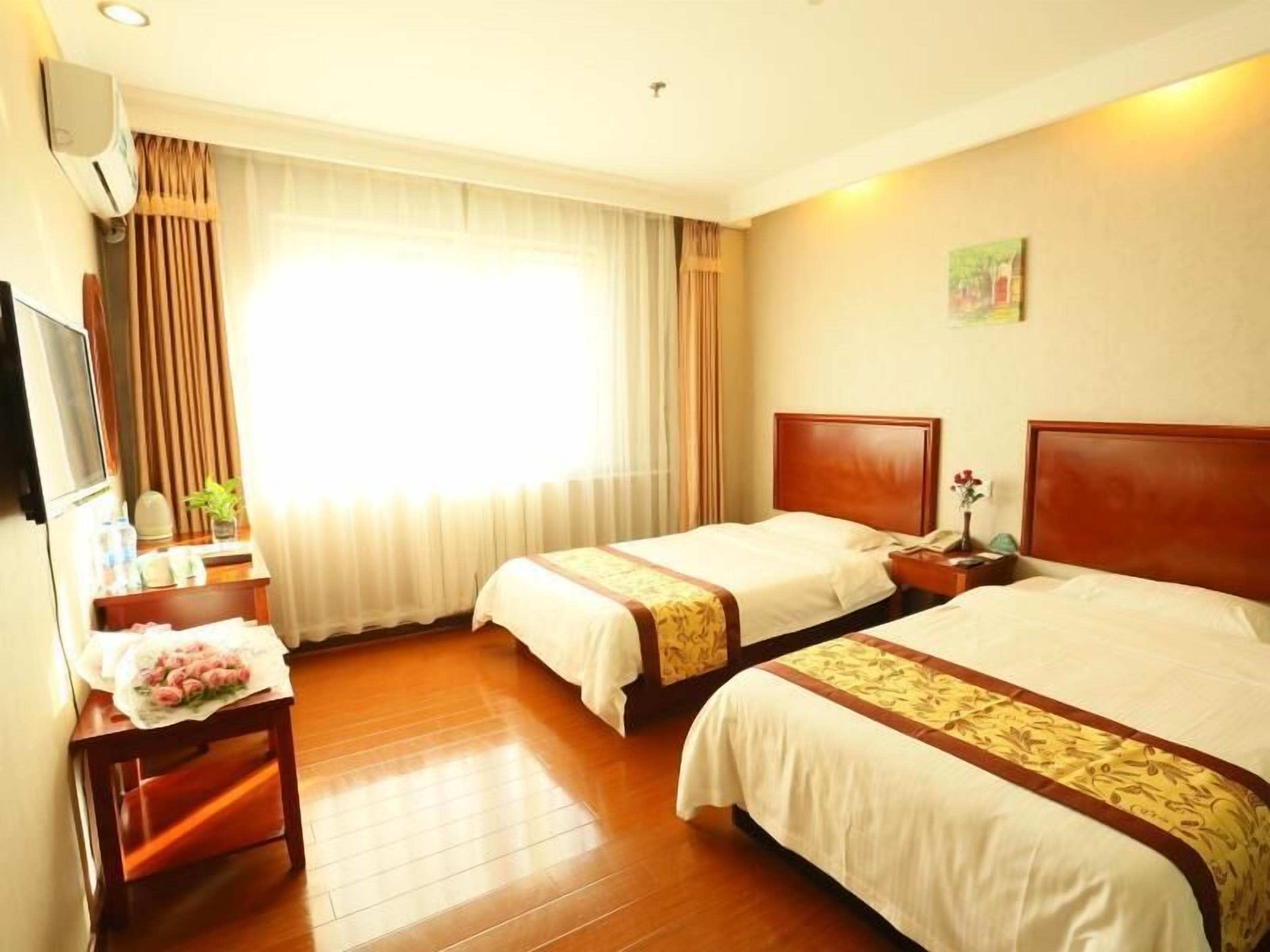 Quarto de hotel com duas camas, uma mesa com televisão, janela com cortinas e um quadro fixado na parede.