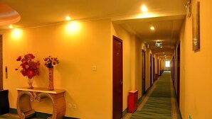 A hotel hallway with a carpeted floor, a wooden console table with a vase of flowers, and doors along the corridor. - Greentree Inn Beijing Changping Shahe Metro Station Express Hotel (Changping)