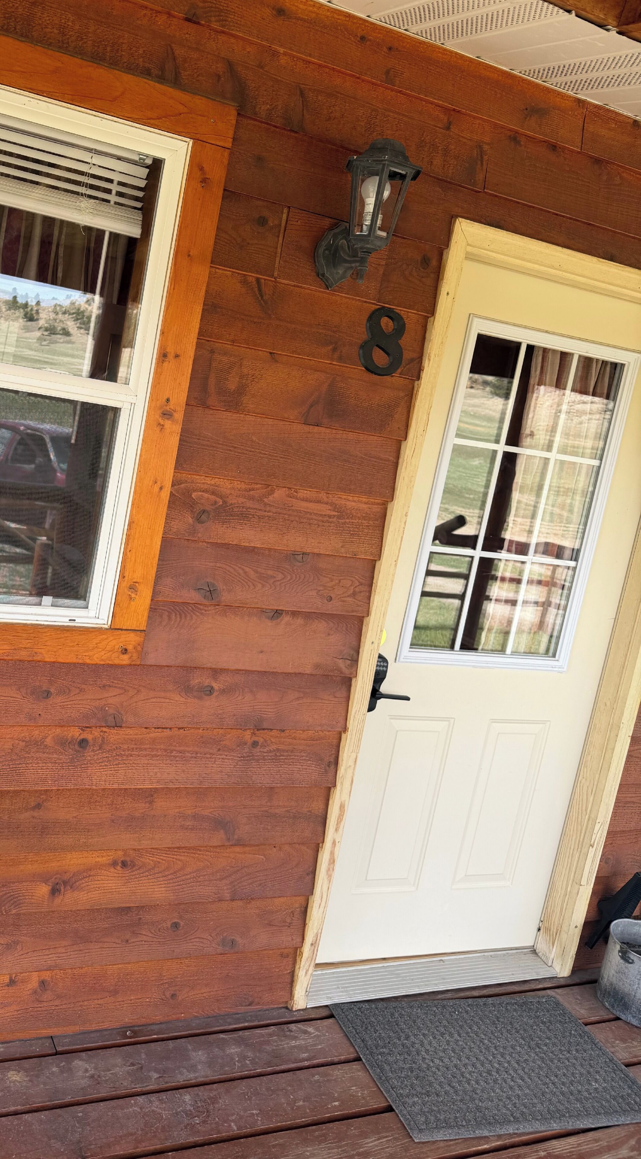 Une maison en bois avec une porte blanche, une fenêtre avec des stores et le chiffre « 8 » peint sur le mur.