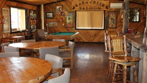 Un rústico espacio de bar con muebles de madera, una mesa de billar y un letrero que dice "Kara Creek Saloon".