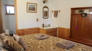 Un dormitorio con una cama, almohadas, un aparador de madera, un tocador con espejo y una ventana.