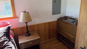 Una habitación con un aparador de madera, una lámpara, un cuadro en la pared y una ventana con cortinas.