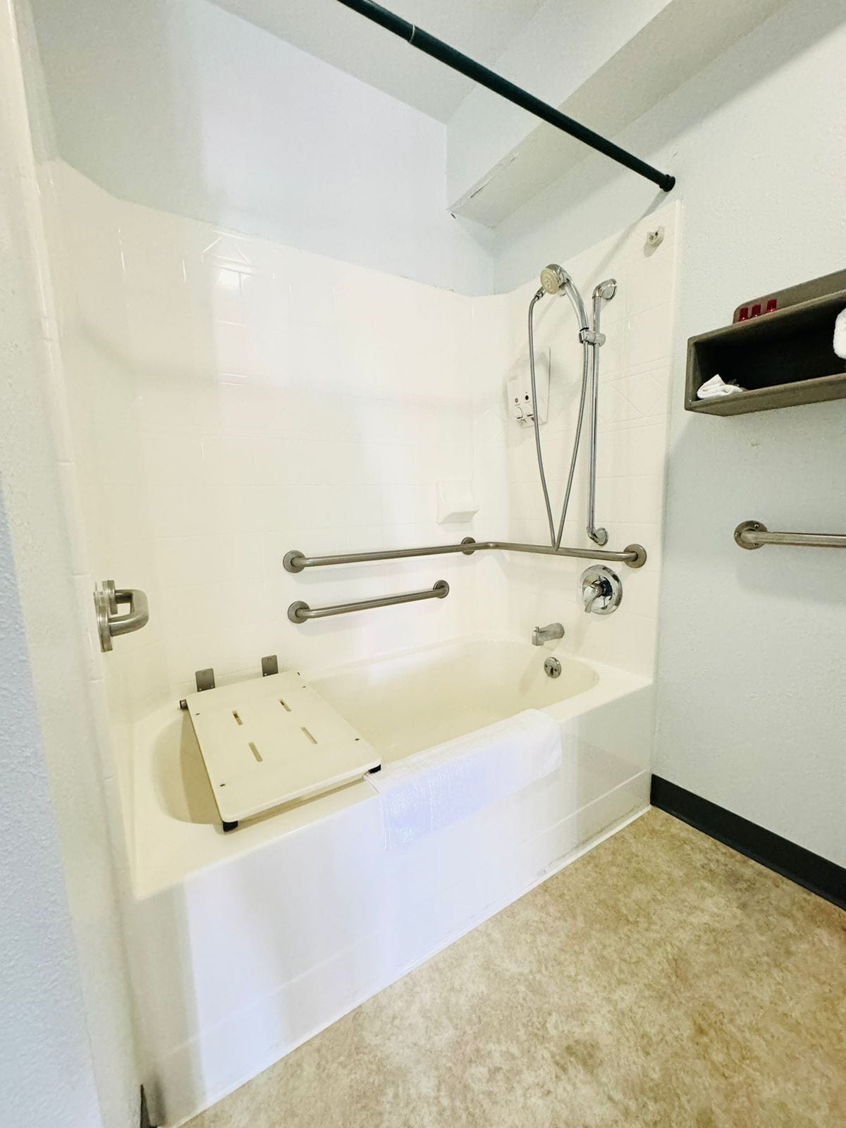 Un baño con una bañera blanca, barras de apoyo, un cabezal de ducha manual y un perchero para toallas.