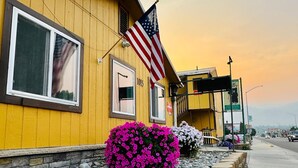 A yellow building with a number '1015' on the door, an American flag, and pink and white flowers in front. - Americas Best Value Inn Salmon (Salmon)