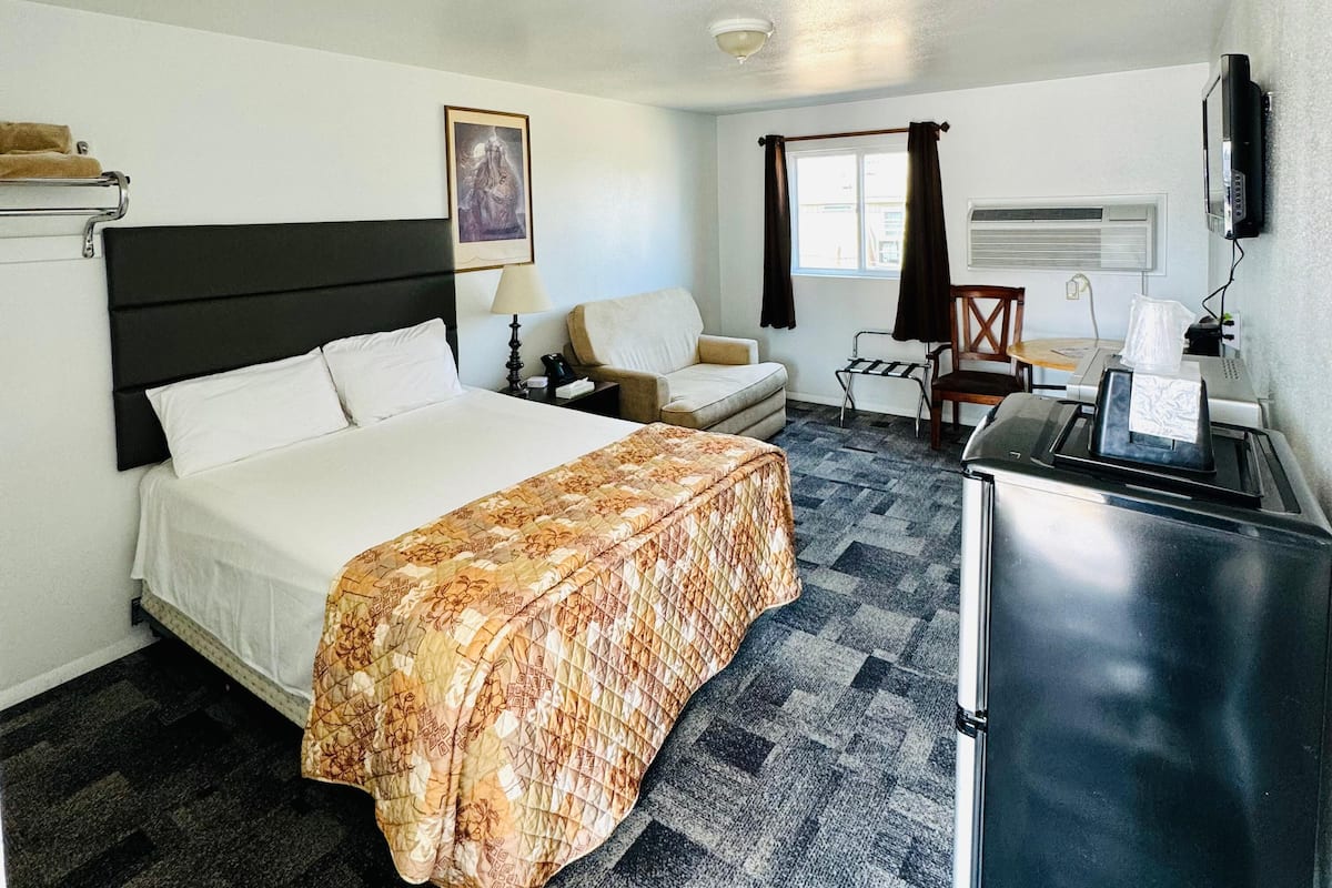 A hotel room with a bed, a desk, a chair, a TV, and a window with curtains.