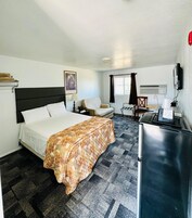 Quarto de hotel com cama, escrivaninha, cadeira, televisão e janela com cortinas.