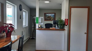 A reception area with a wooden counter, a coat rack, a plant, and a door with a bell. - Americas Best Value Inn Salmon (Salmon)