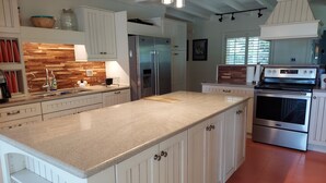 A kitchen with white cabinetry, a granite countertop, stainless steel appliances, and a wooden backsplash.