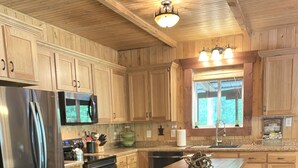 A kitchen with wooden cabinets, a stainless steel refrigerator, a microwave, and a wooden island with stools. - Experience the peaceful Wooded Retreat Cabin - 300 private acres -security gate  (Spencer)