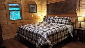 A wooden cabin bedroom with a bed, two bedside lamps, a window, and a ceiling fan. - Experience the peaceful Wooded Retreat Cabin - 300 private acres -security gate  (Spencer)