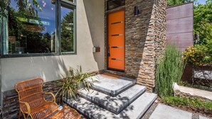 A modern house with a stone facade, an orange door, and a set of steps leading to the entrance.