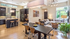 A modern kitchen with dark cabinetry, a central island, and a dining area with a large table and chairs.