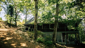 Une maison à deux étages avec un porche, entourée d’arbres et bordée d’un chemin de gravier.