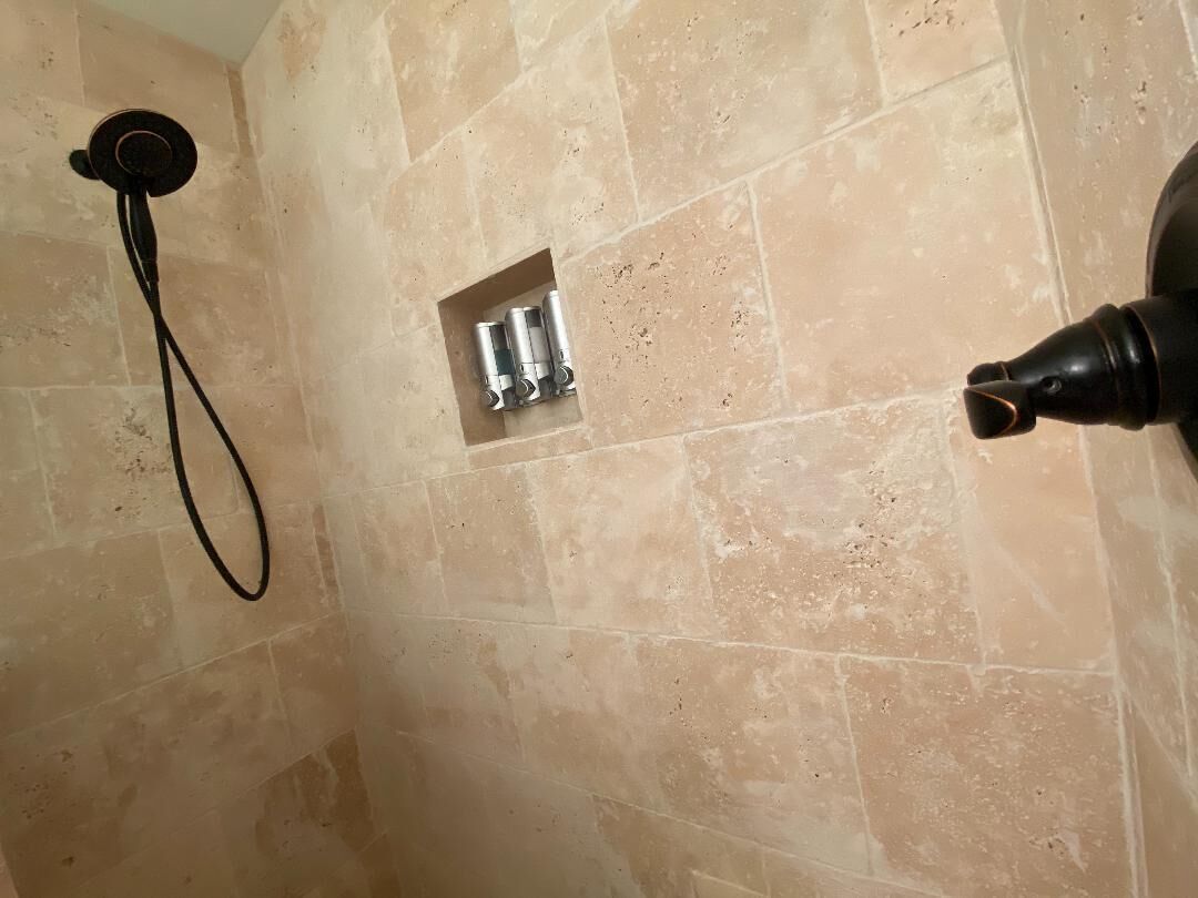 A bathroom with beige tiles, a showerhead, and a faucet.