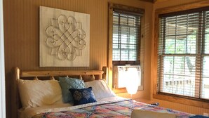 A wooden cabin bedroom with a bed, a quilt, and a window with blinds.
