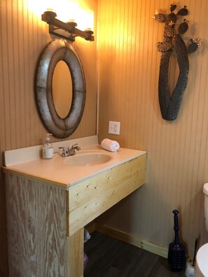 A bathroom with a wooden vanity, sink, and mirror, featuring a unique wall decoration and a striped pattern.