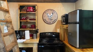 A kitchen with a stove, microwave, and wooden shelves with red dishes.
