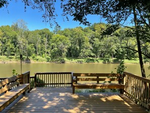 A wooden deck with benches overlooking a calm lake surrounded by dense trees.